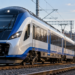 AI-generated editorial illustration of a blue-and-white modern passenger train in a European railway setting; not a verified PESA model or a train operating in India